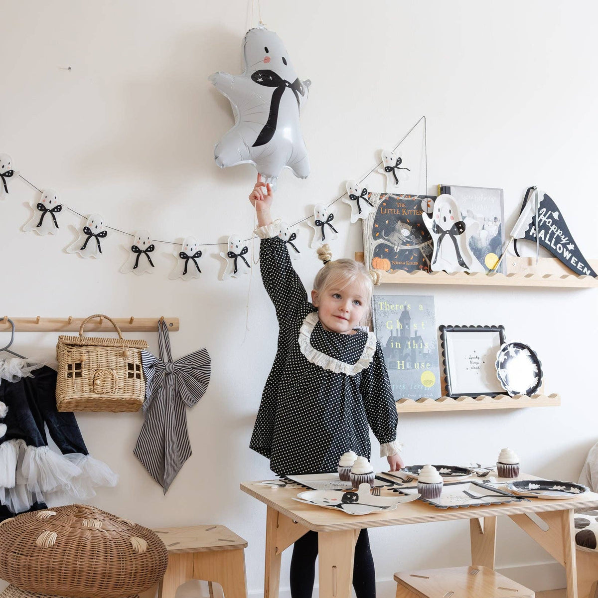 Ghost mylar balloon and ghost garland styled in a kids Halloween playroom with a set table and cupcakes