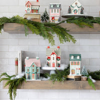 Retro Christmas decor village collection styled on two white kitchen shelves with garland, showing multiple houses and a church.