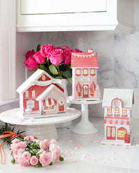 Full set of the valentine village houses displayed on a counter, with the sweet shoppe decor glowing and surrounded by pink roses.