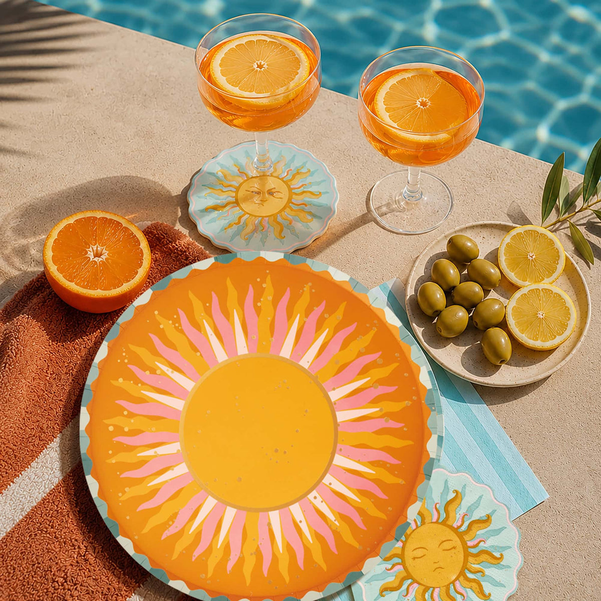 Sun shaped paper cocktail napkins styled poolside under orange spritz cocktails with a sunburst plate and citrus.