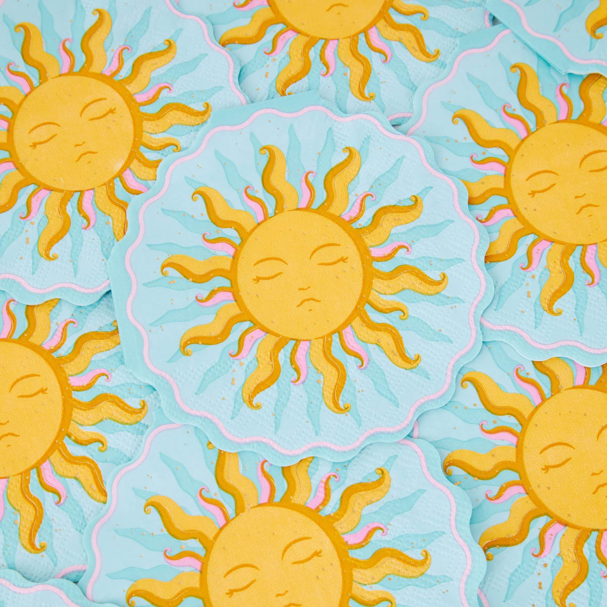 Overlapping sun shaped cocktail napkins showing the gold sun face, sky blue ground, and scalloped die-cut edge.