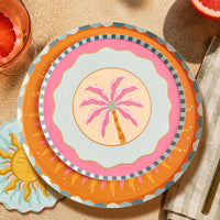 Sunburst dinner plate layered under a pink palm plate with orange cocktails and olives on a sunny table.