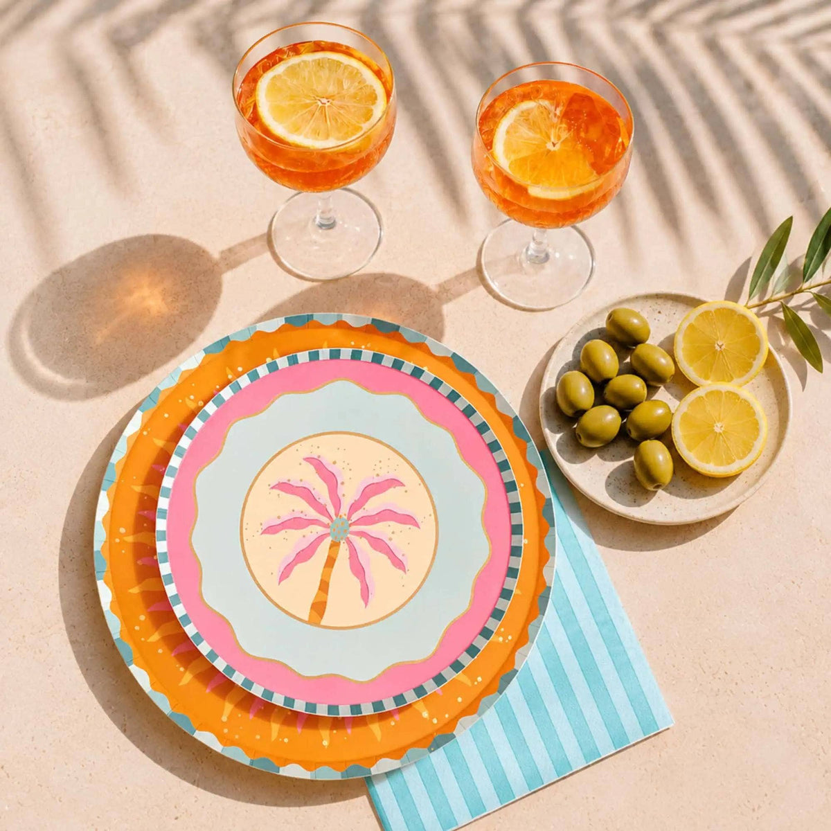 Orange sunburst paper dinner plate beside sun-shaped napkins, a palm plate, and blue striped napkins.