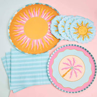 Orange and pink sunburst paper dinner plates angled in a group, showing the golden center and teal scalloped edge.