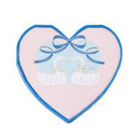 Heart shaped paper napkin with two white swans under a blue bow, pink ground with cobalt border and gold foil detail