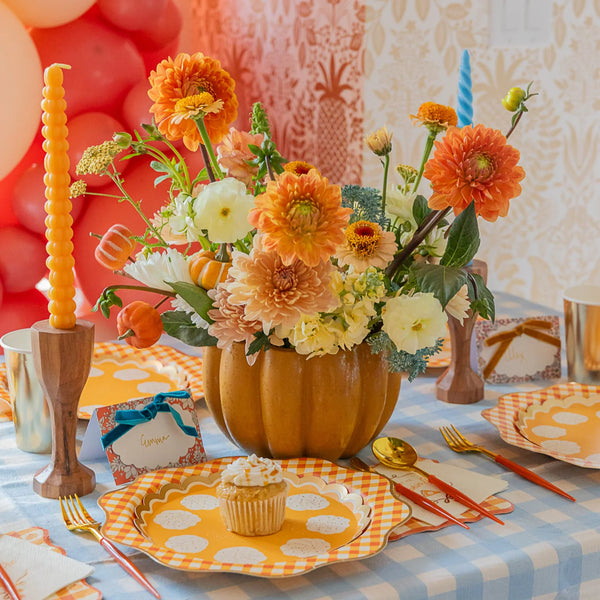 Close place setting showing orange gingham charger layered under a pie-print dessert plate with a cupcake.