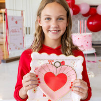 Girl holding pink heart charm plate at a Valentine-themed party setup.