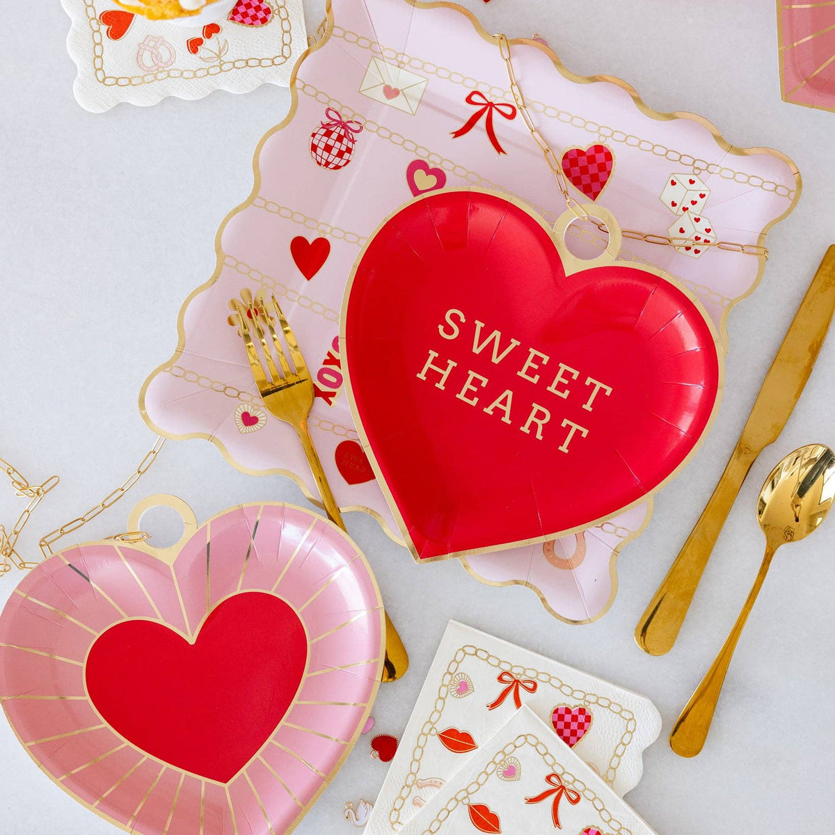 Flatlay of red and pink heart plates with coordinating Valentine’s tableware.