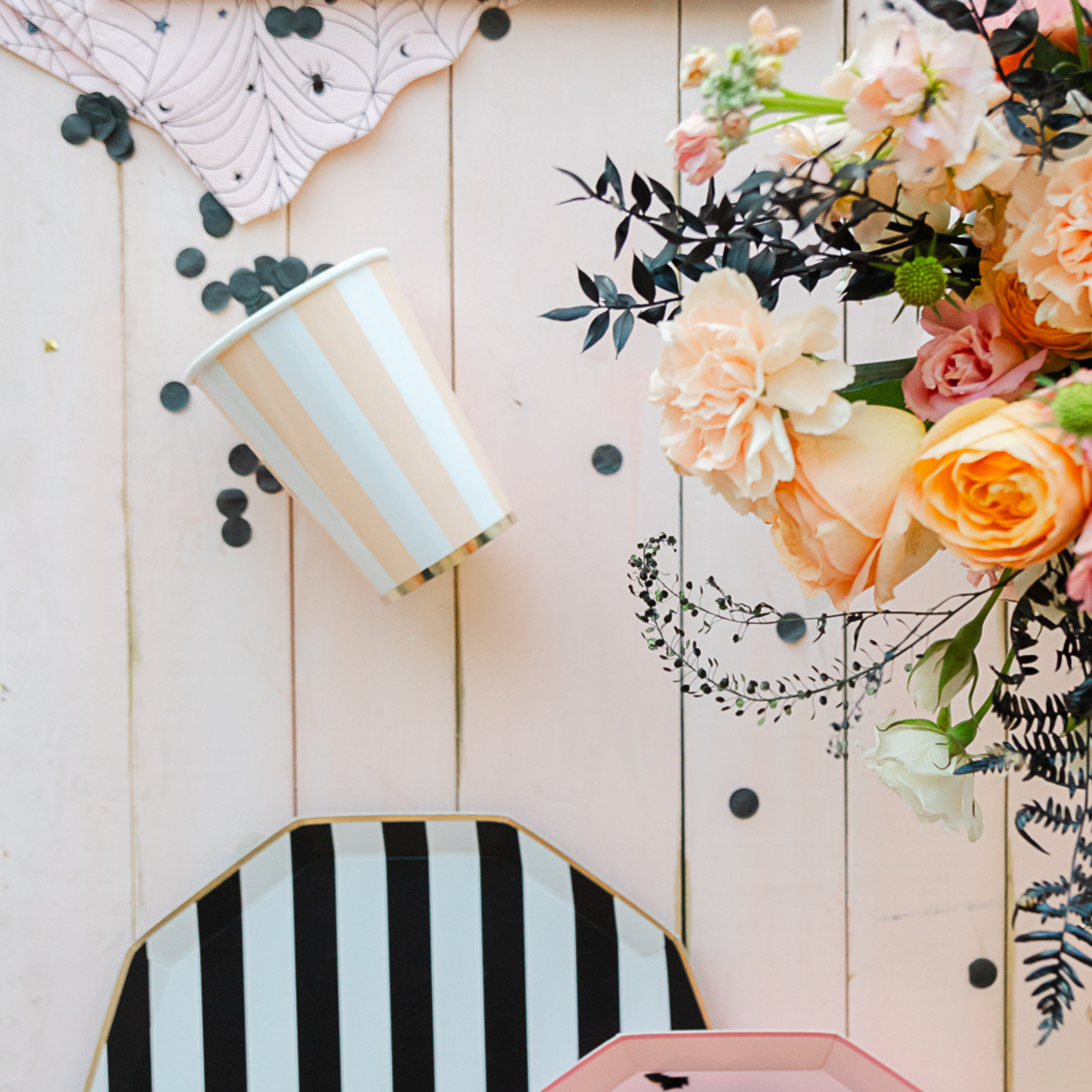 Peach cabana stripe cup on pink wood table with floral arrangement