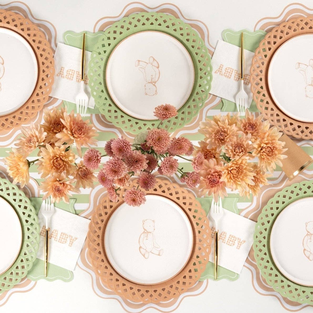 Overhead tablescape showing sage napkins with bunny plates, green and tan scalloped chargers, and orange florals.