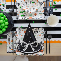 Halloween-themed table setting with decorative plates, cups, and utensils on a striped tablecloth.