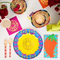 This image shows a taco-themed party table with colorful plates, sombreros, flowers, and fiesta decorations.
