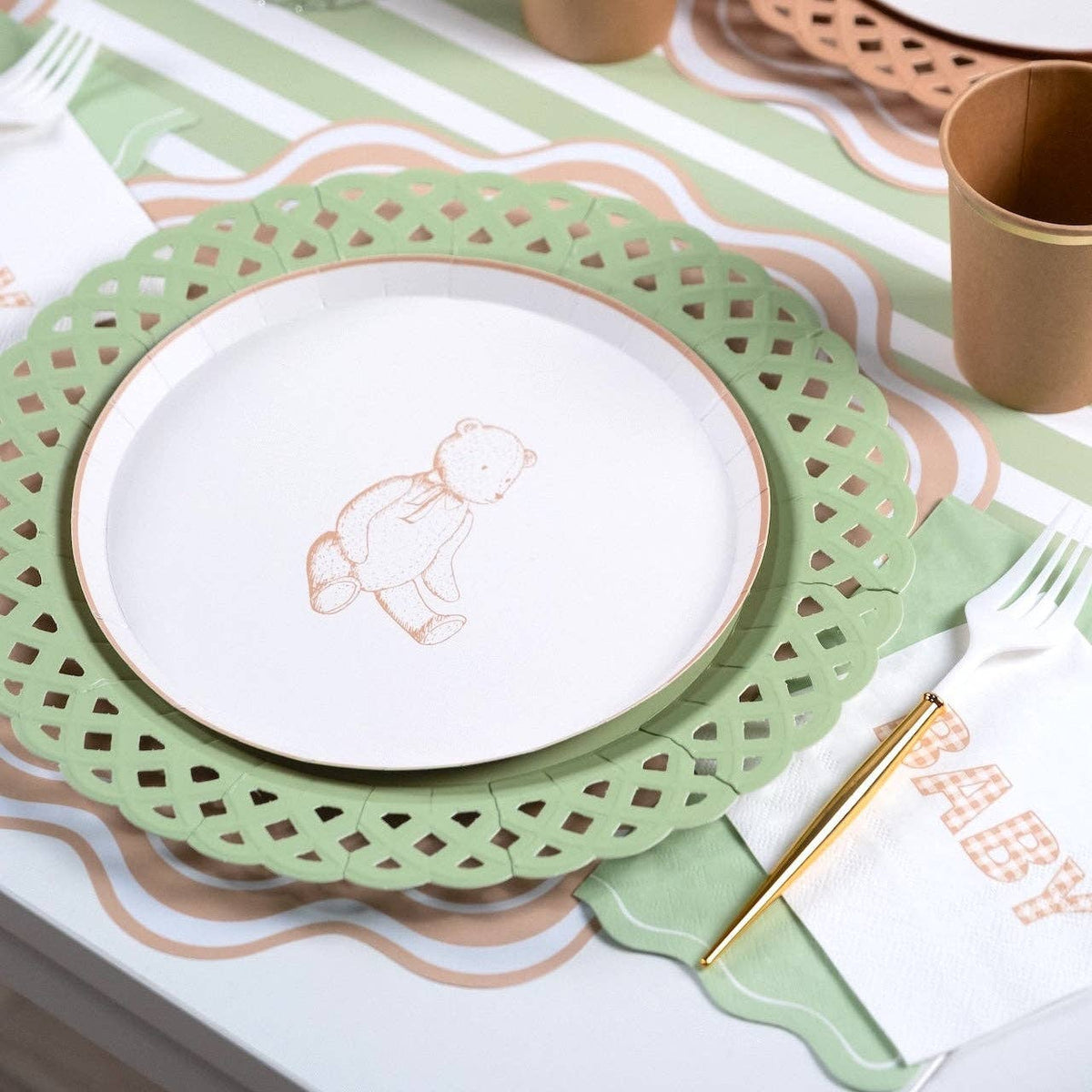 Tan gingham BABY napkin beside a teddy bear plate on a sage green lattice charger with a gold fork
