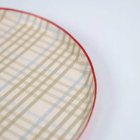 Corner close-up of a tan plaid paper dinner plate showing the check pattern and red rim.