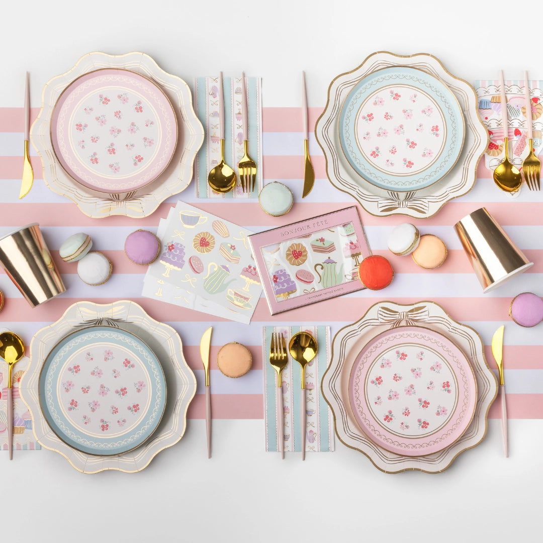 Styled tea party place setting showing the tower napkins with scalloped plates, gold flatware, and pastel décor on a striped runner.