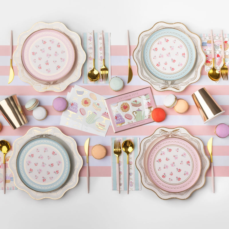 Styled tea party place setting showing the guest towels with scalloped plates, gold flatware, and pastel décor on a striped runner.