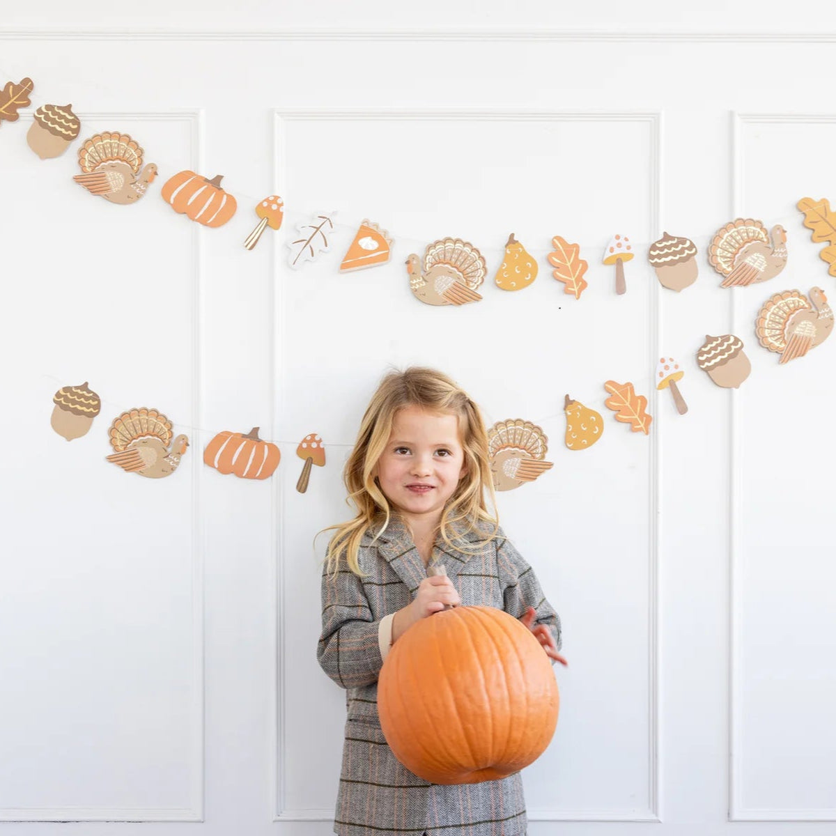 Child standing in front of hung Thanksgiving icons banner on a white wall.