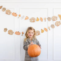 Child standing in front of hung Thanksgiving icons banner on a white wall.