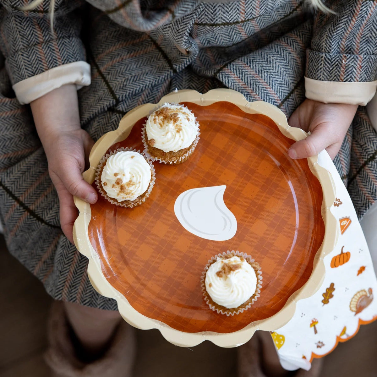 Child holding a dessert plate with an icons napkin peeking out on their lap.