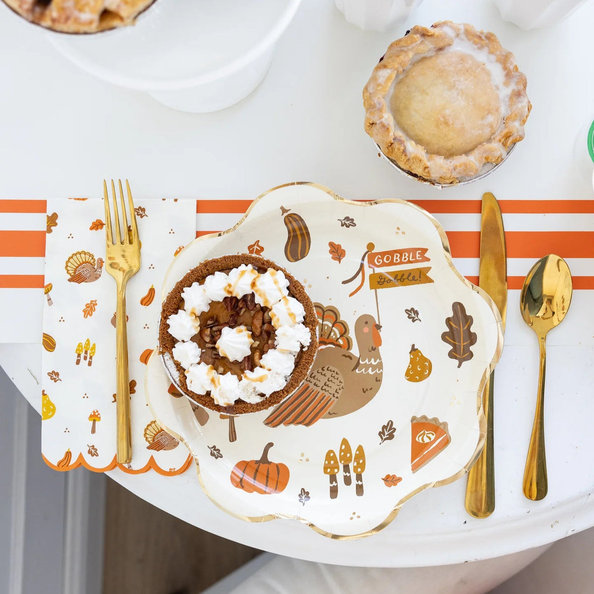 Thanksgiving place setting with turkey plate, gold flatware, and icons napkin.