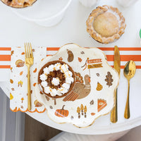 Thanksgiving place setting with turkey plate, gold flatware, and icons napkin.