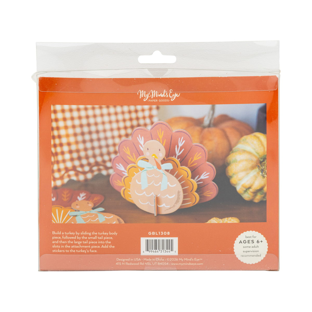 Package of a turkey craft kit with pumpkins and checkered tablecloth in the background, back view.