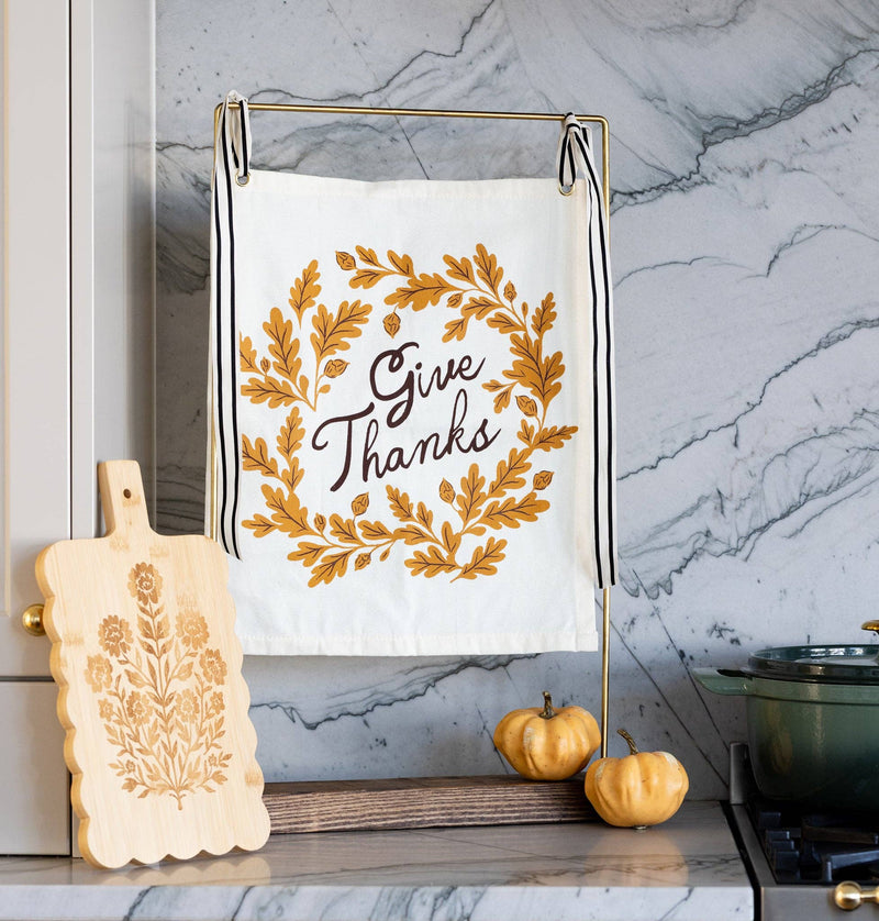 Styled Thanksgiving kitchen decor showing the Give Thanks canvas banner hanging from a brass countertop stand next to mini pumpkins.