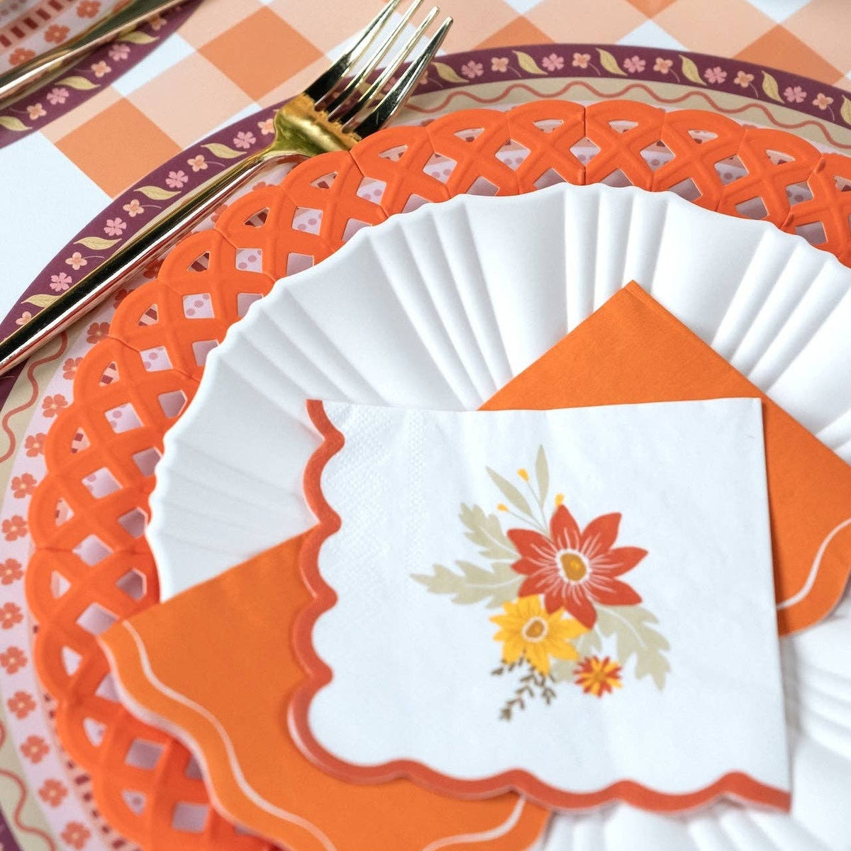 Thanksgiving place setting with the orange guest towel and a fall floral napkin on an orange cutwork lattice charger over an orange-and-white gingham table.