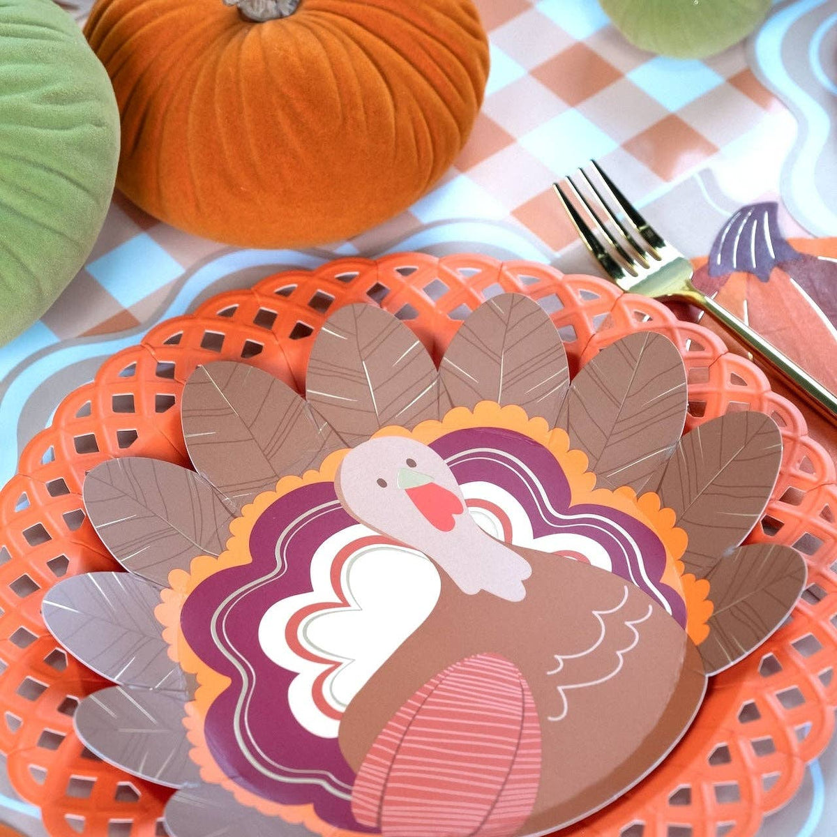 Styled Thanksgiving place setting showing the turkey plate layered on orange and floral plates with a pumpkin and gingham runner.