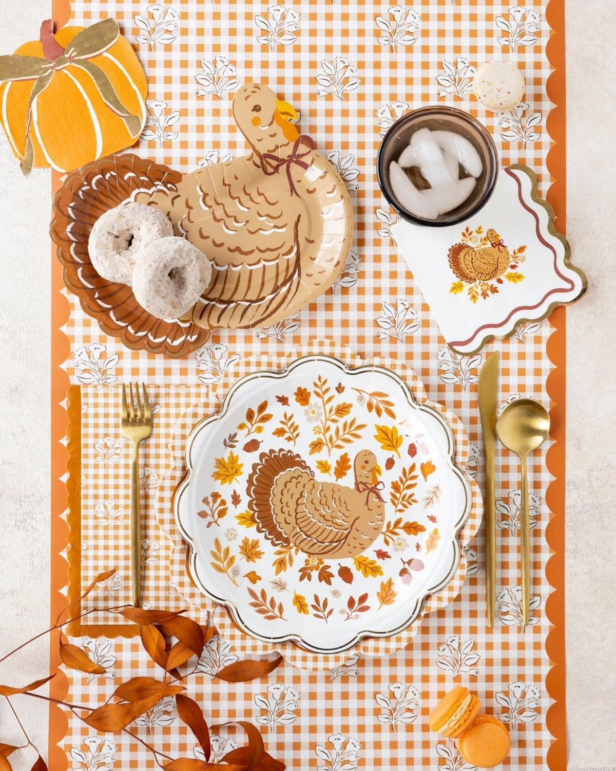 Styled Thanksgiving table overhead shot showing the rust gingham runner as the base layer under harvest plates, a turkey-shaped plate, woven placemats, pumpkins, and fall décor on a wood table.