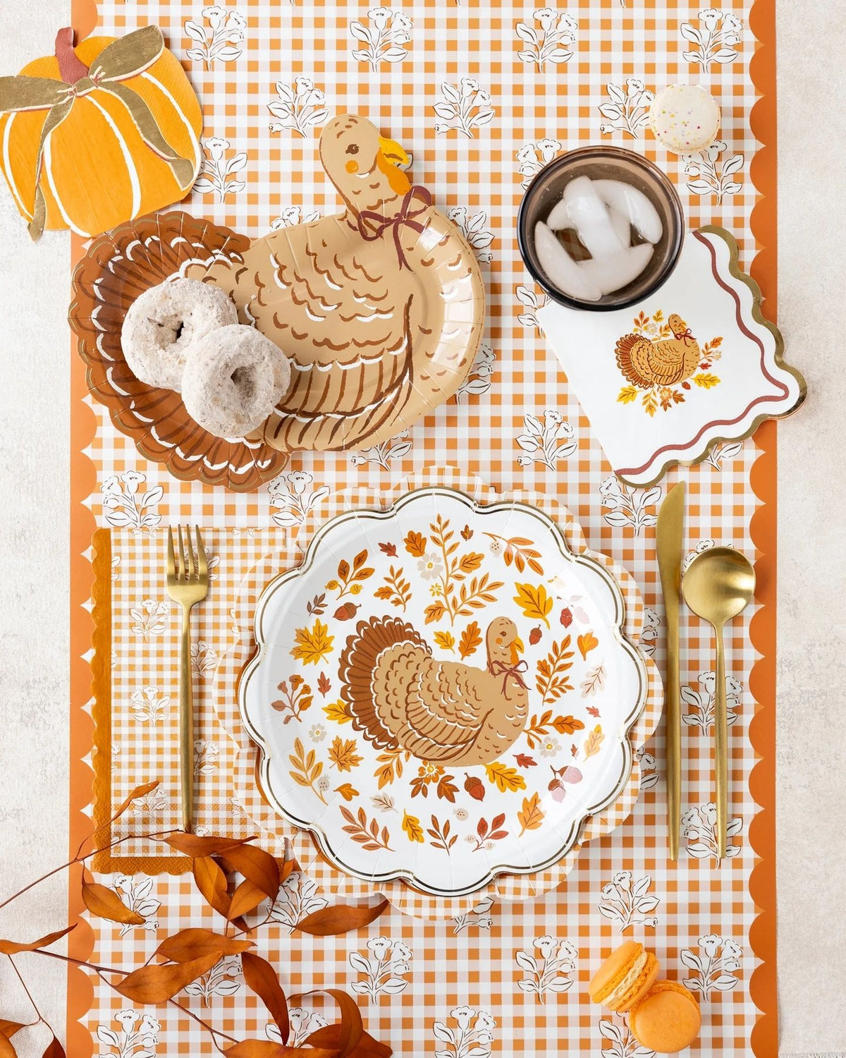 Styled Thanksgiving table overhead showing the turkey foliage plate as the centerpiece on the rust gingham block-print runner, with pumpkins, woven elements, and autumn décor.