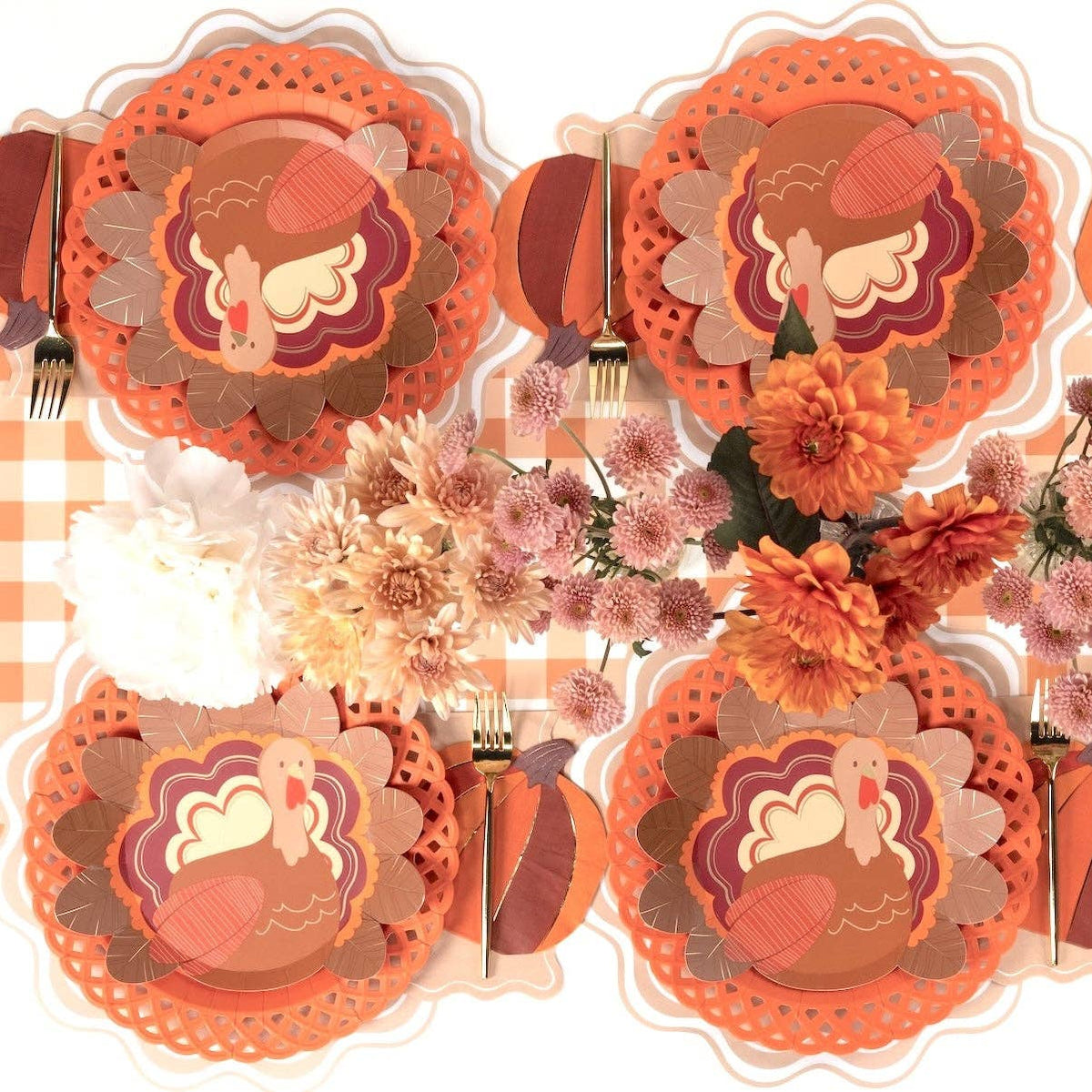 Overhead Thanksgiving tablescape showing turkey plates on orange chargers with floral plates, autumn florals, and gold flatware on a gingham runner.