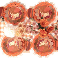 Overhead Thanksgiving tablescape showing turkey plates on orange chargers with floral plates, autumn florals, and gold flatware on a gingham runner.
