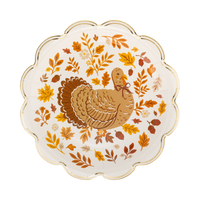 Cream round Thanksgiving dinner plate with a detailed brown turkey illustration in the center surrounded by a wreath of fall leaves, acorns, and berries, with a gold foil scalloped edge, overhead view.