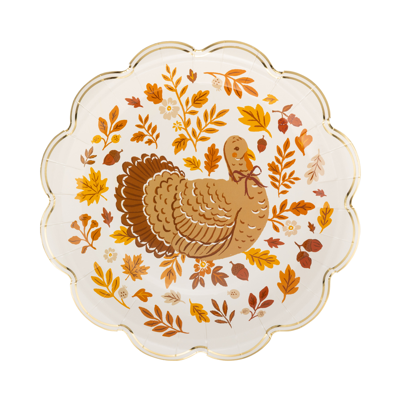 Cream round Thanksgiving dinner plate with a detailed brown turkey illustration in the center surrounded by a wreath of fall leaves, acorns, and berries, with a gold foil scalloped edge, overhead view.