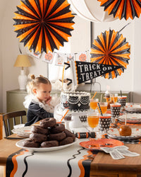 Halloween-themed party setup with decorations, food, and a child at a table showcasing the tissue paper fans.