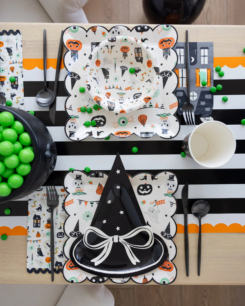 Halloween-themed table setting with decorative plates, cups, and utensils on a black and white striped tablecloth.