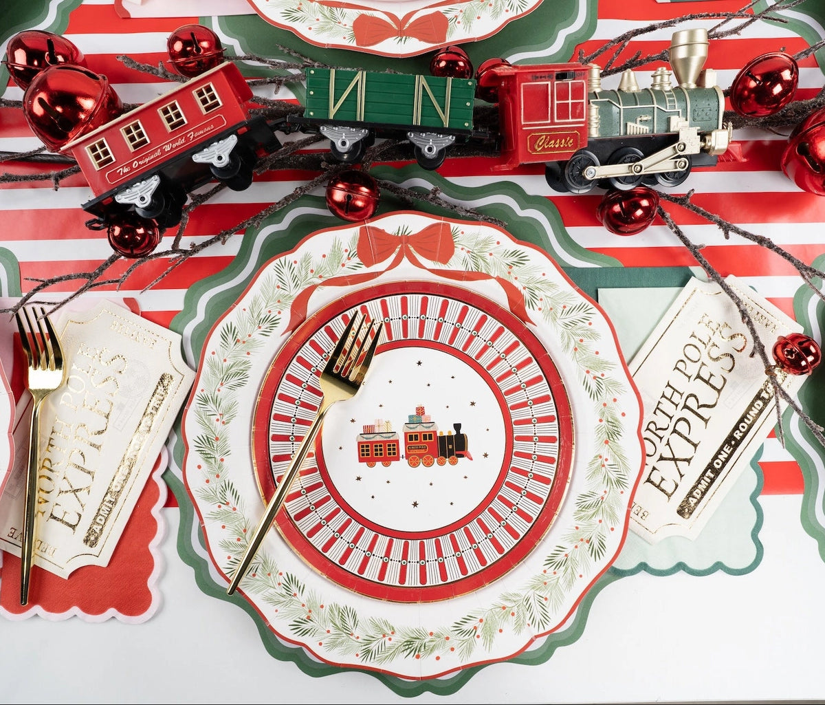 Place setting with a toy-train plate on the wreath dinner plate and green charger, with a "North Pole" banner and red ornaments.