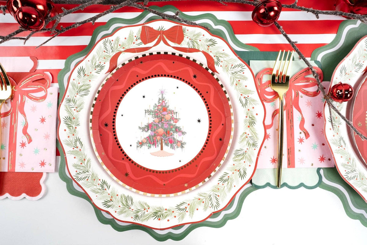 Place setting with the tree plate on scalloped red and evergreen-rim plates, gold cutlery, and a red bow napkin.