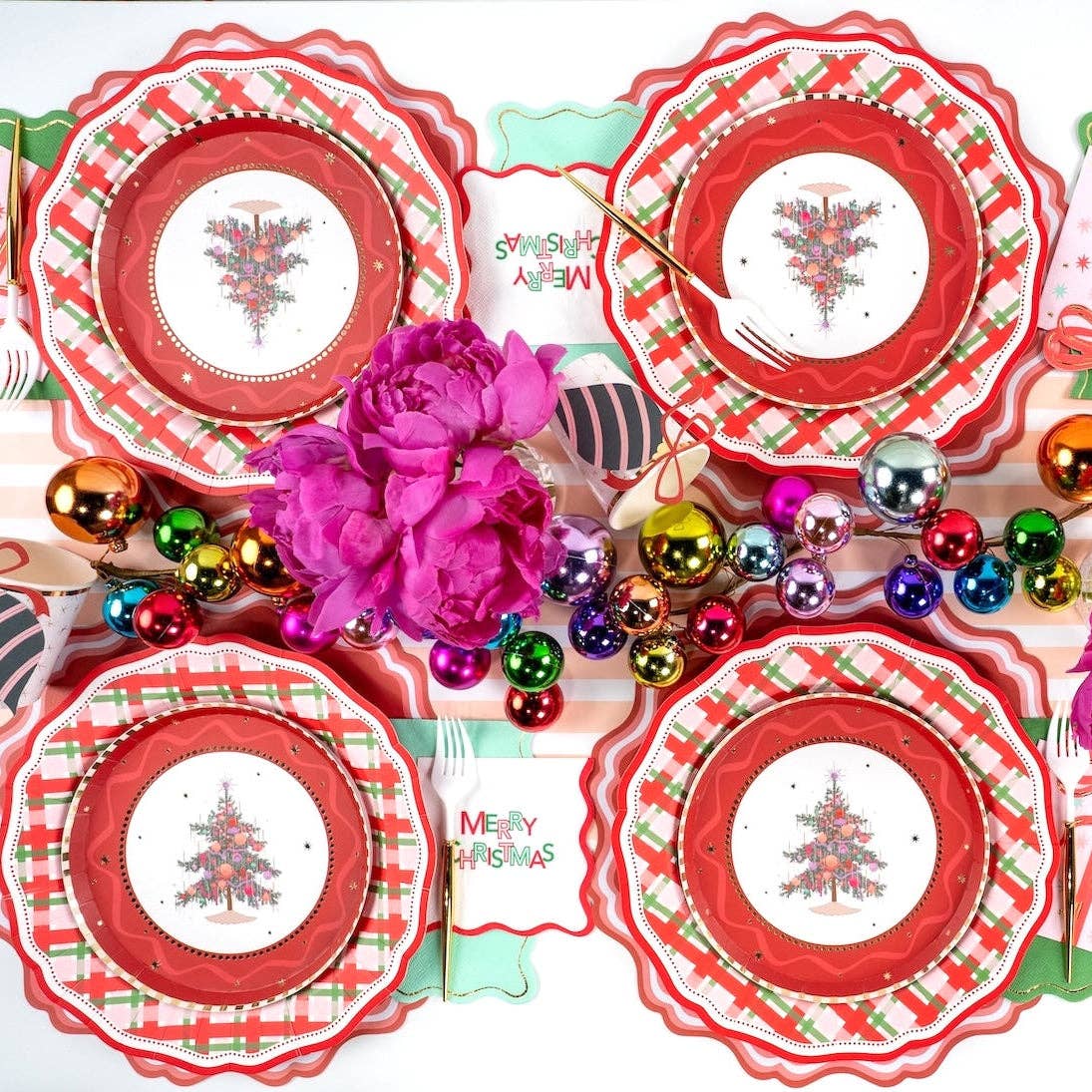Overhead of four tree plates on red scalloped plates around pink peonies and a "Merry Christmas" napkin.