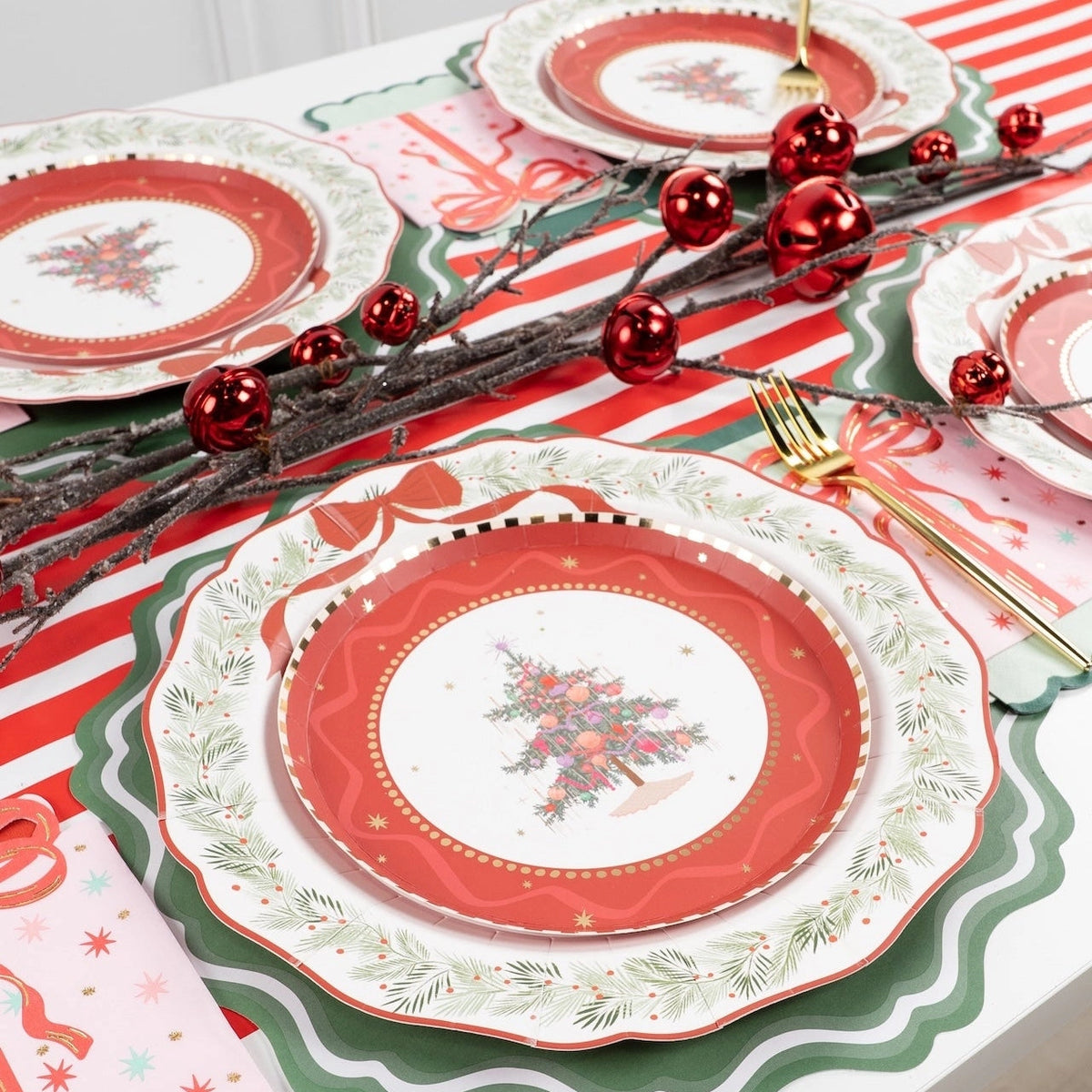 Overhead of tree and train plate settings on wreath dinner plates with a red-and-white striped runner and red ornaments.