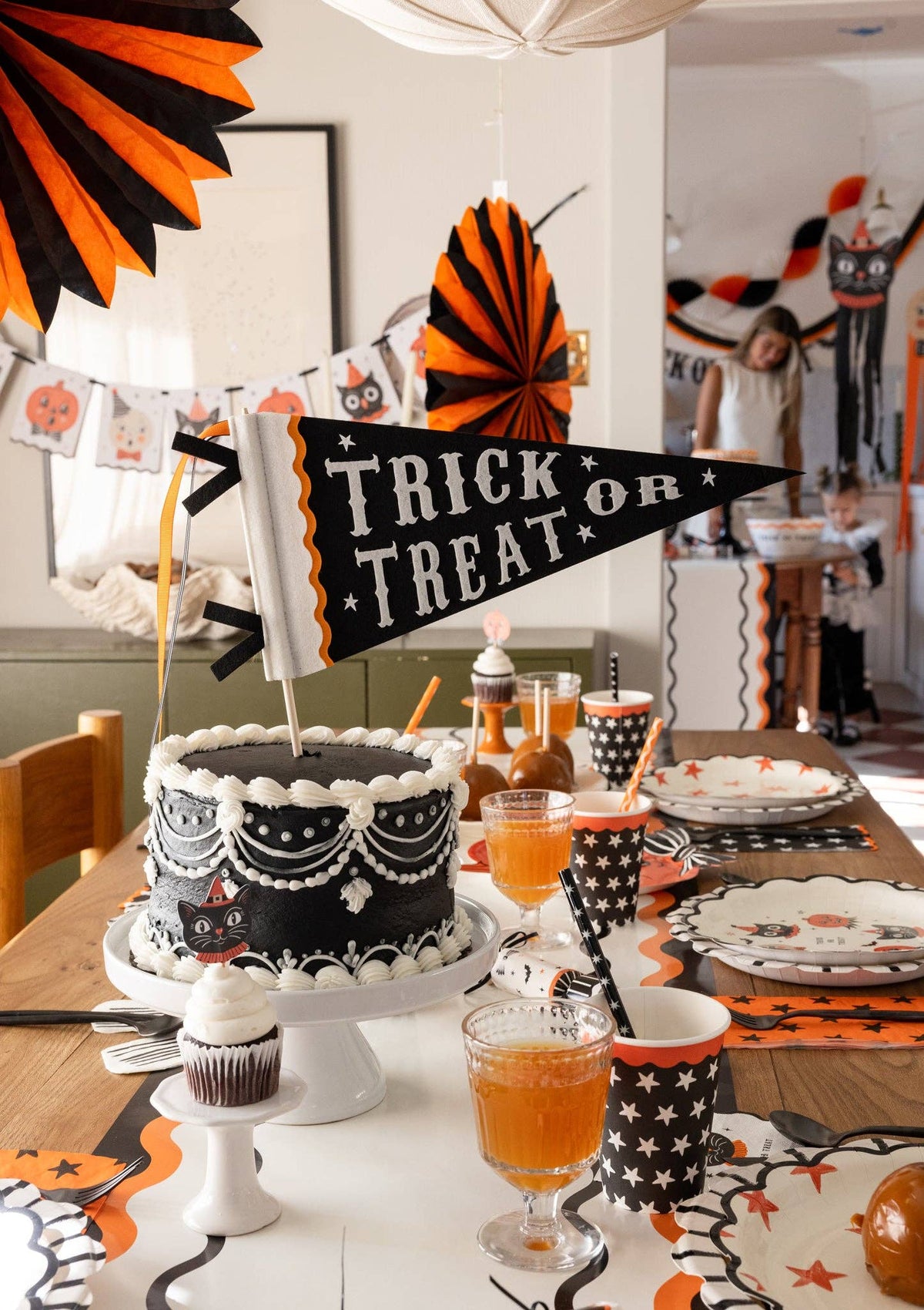 Halloween-themed table setting with cake, drinks, and decorations with a closer view of Trick or treat felt pennant.