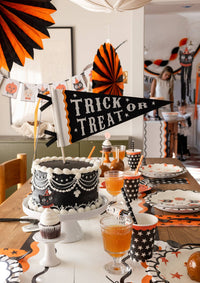 Halloween-themed table setting with cake, drinks, and decorations with a closer view of Trick or treat felt pennant.