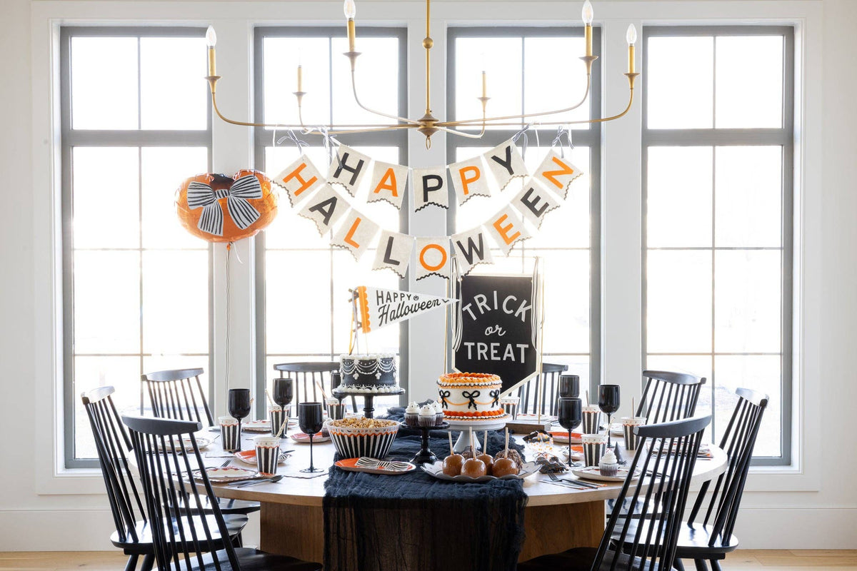 Halloween dessert table with the Trick or Treat felt banner, Happy Halloween banner, striped cups, black glassware and caramel apples
