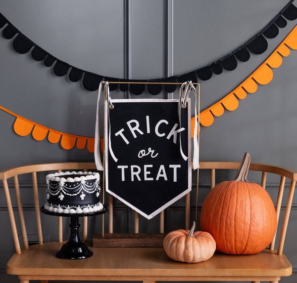 Black felt Trick or Treat banner hanging on a gold stand beside a black and white piped cake and two pumpkins