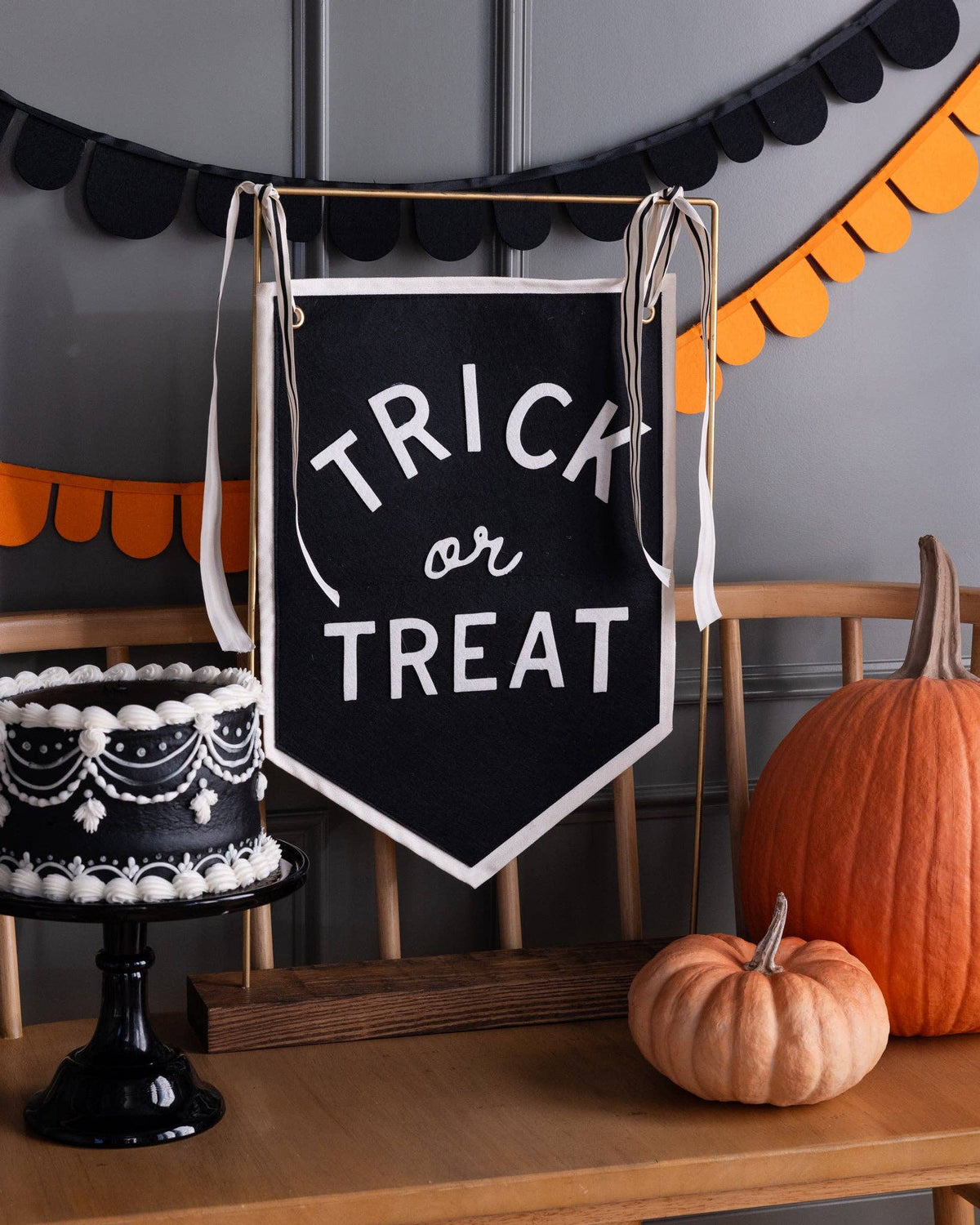 Trick or Treat felt banner styled with black and orange scalloped felt garlands, a black cake and orange pumpkins