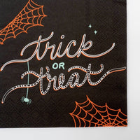 Close-up of the trick or treat napkin showing the white script lettering, orange spiderweb corner, and dangling spider detail.