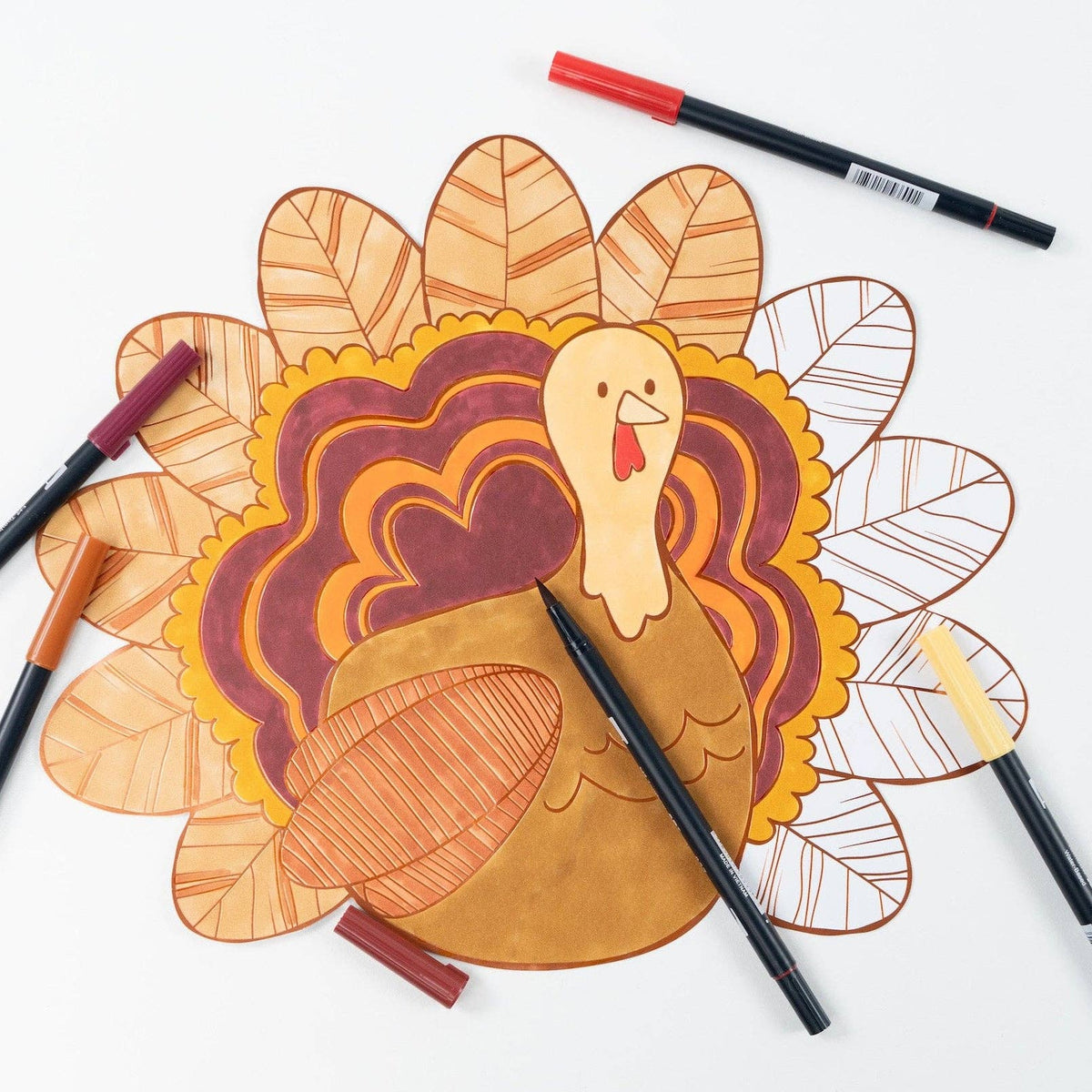 The coloring placemat with markers laid on top, showing the turkey partly colored in rust, burgundy, and orange.