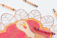 Close-up of the turkey coloring placemat showing a pink-and-orange colored turkey with markers beside it.