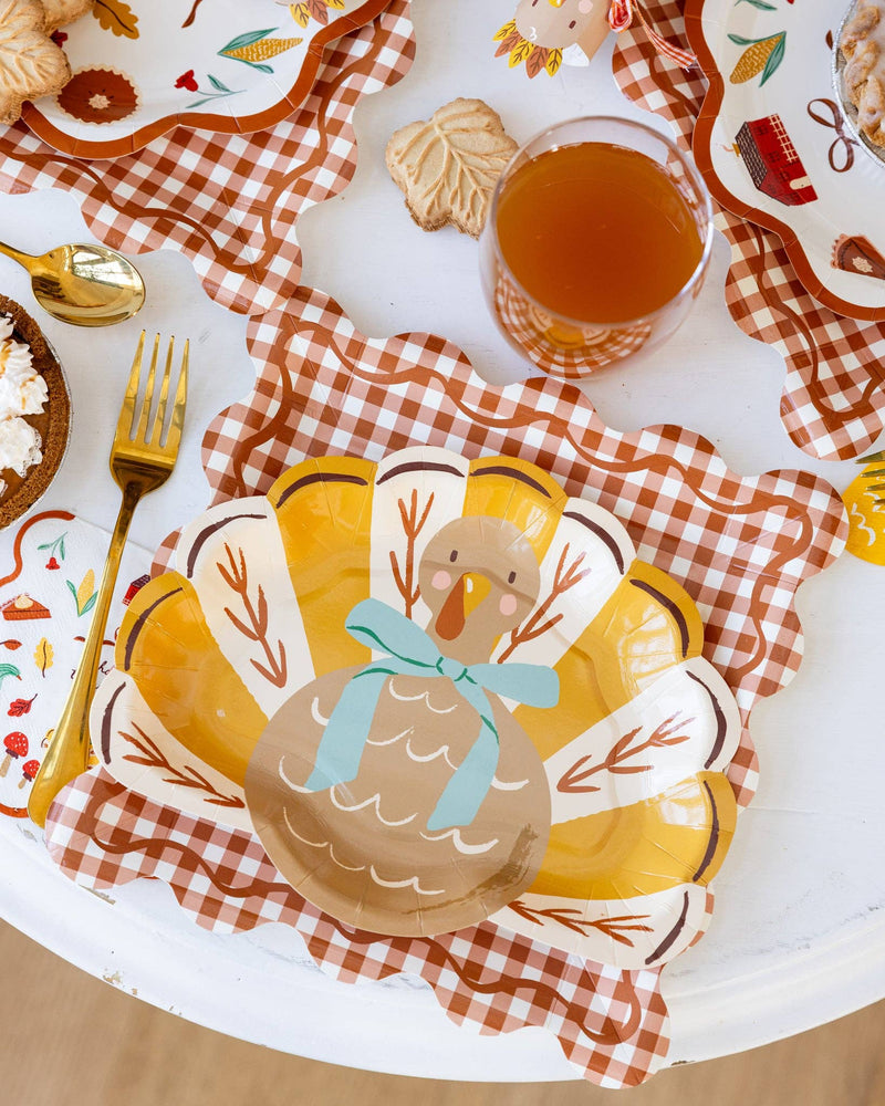 Thanksgiving-themed place setting with turkey paper plate, glass of juice, and checkered charger plate.
